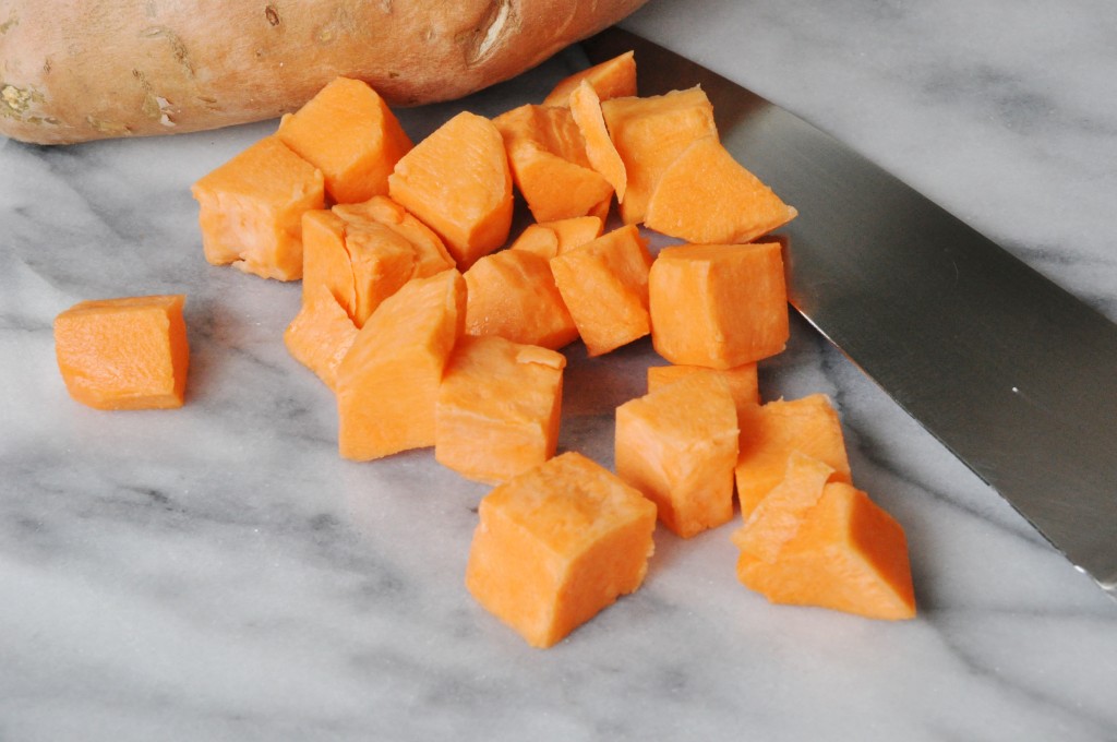 Sweet potatoes chopped on a marble board with a chef's knife next to the potatoes