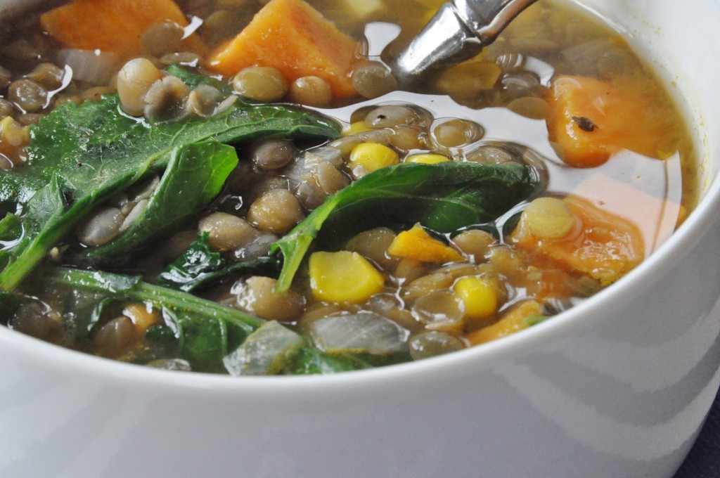 A close up of vegetable soup in a white bowl with a silver spoon in the bowl