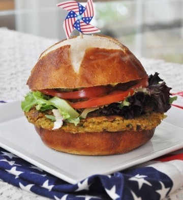 A chickpea burger with lettuce and tomato on a square white plate that's sitting on an American flag napkin.