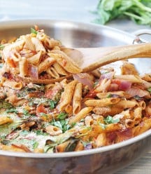 Vegan Penne Pasta Casserole in a round copper pan with a wood spoon taking some out of the pan
