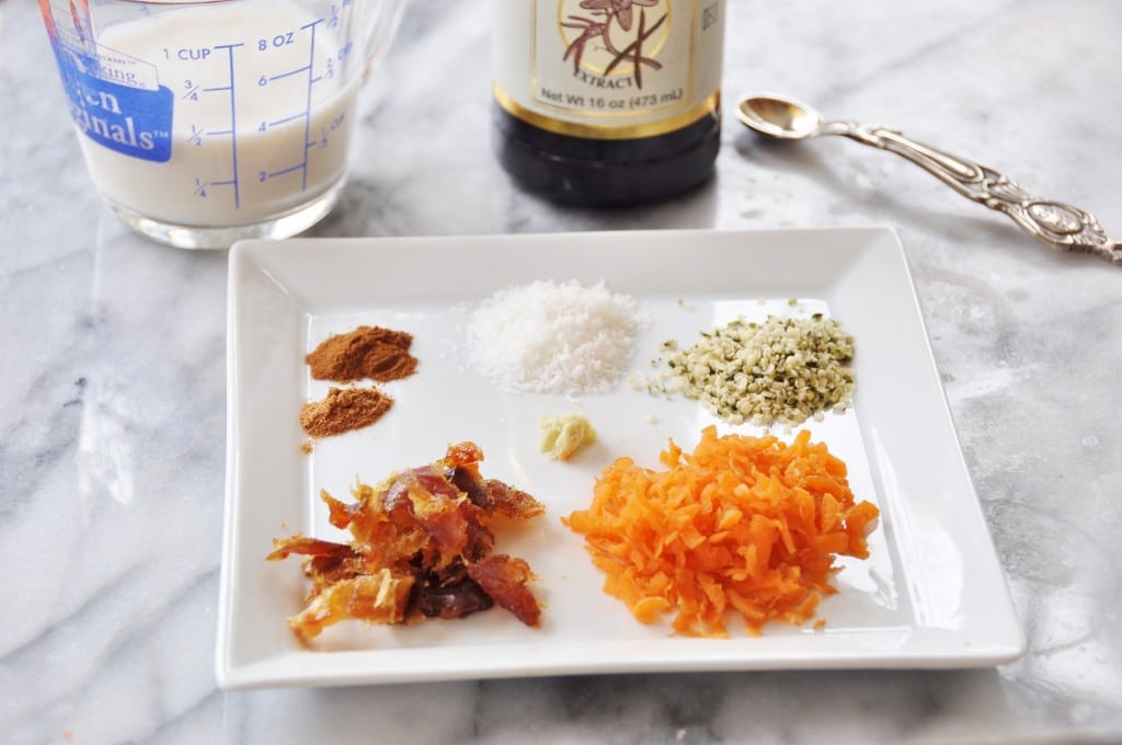 Spices for Carrot Cake Overnight Oats on a white plate with a measuring cup of milk and a bottle of vanilla in the background