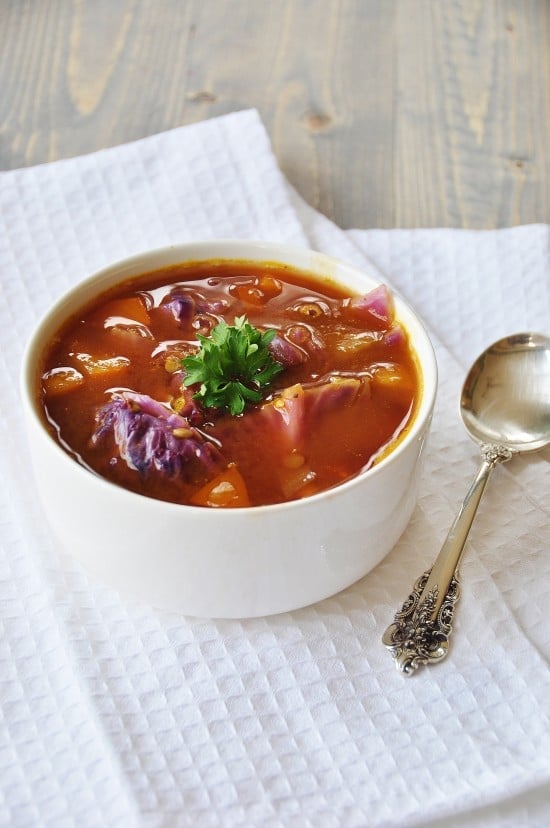 Red Cabbage and Green Lentil Soup in a white bowl on a white towel with a silver spoon next to the bowl. 