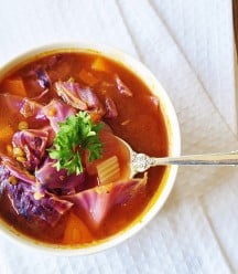 Eine Draufsicht auf Kohlsuppe in einer weißen Schüssel auf einem weißen Handtuch mit einem silbernen Löffel in der Schüssel.