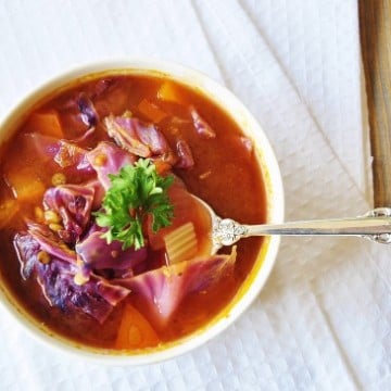 An overhead shot of Cabbage soup in a white bowl on a white towel with a silver spoon in the bowl.