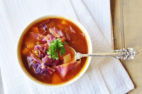 Eine Draufsicht auf Kohlsuppe in einer weißen Schüssel auf einem weißen Handtuch mit einem silbernen Löffel in der Schüssel. 