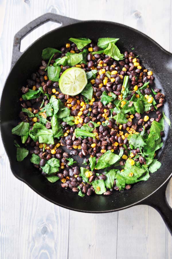 Corn-and-Bean-Hash in an iron skillet with a lime wedge and spinach leaves