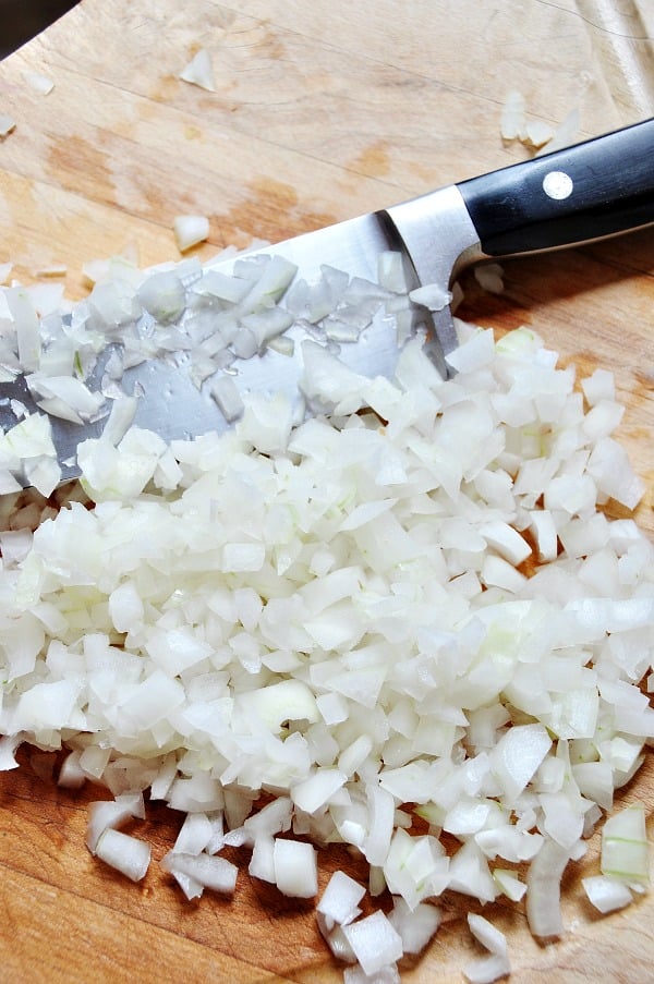 Zwiebelwürfel auf einem Holzbrett mit einem Messer auf dem Brett. 