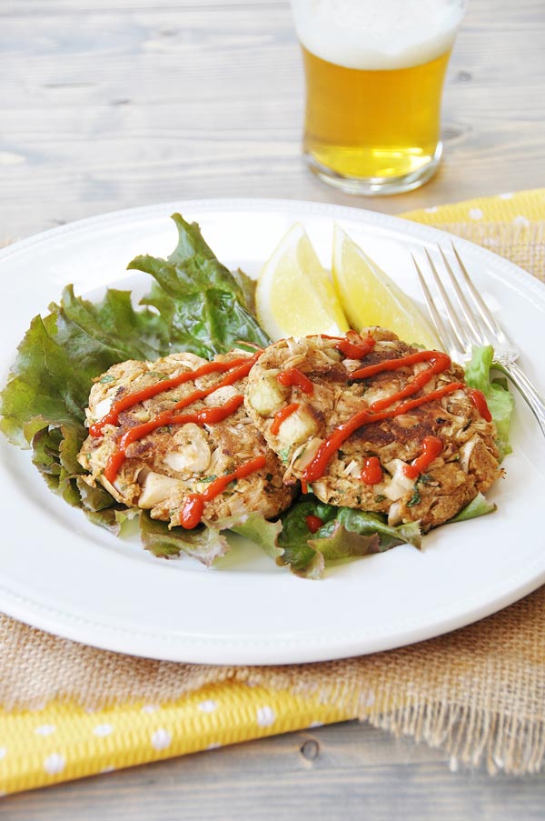 Crab cakes on a bed of lettuce with lemon on a white plate, and a beer next to the plate.