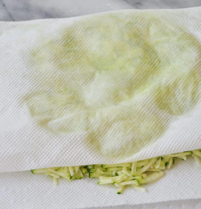 Pressing water out of shredded zucchini between paper towels.