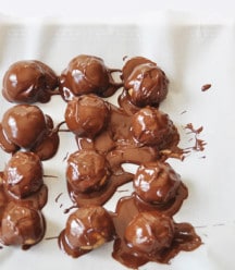 melted chocolate poured over peanut butter balls on a piece of parchment paper.