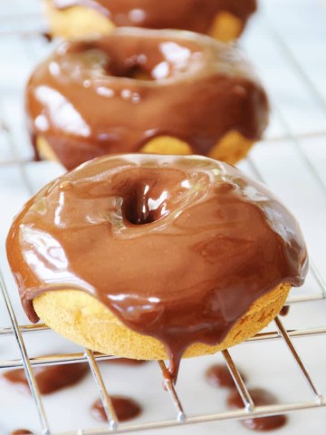 Three pumpkin spice doughnuts with chocolate cinnamon icing covering the tops and dripping down the sides on a wire cooking rack