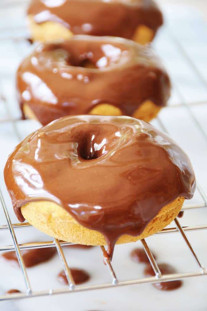 Three pumpkin spice doughnuts with chocolate cinnamon icing covering the tops and dripping down the sides on a wire cooking rack
