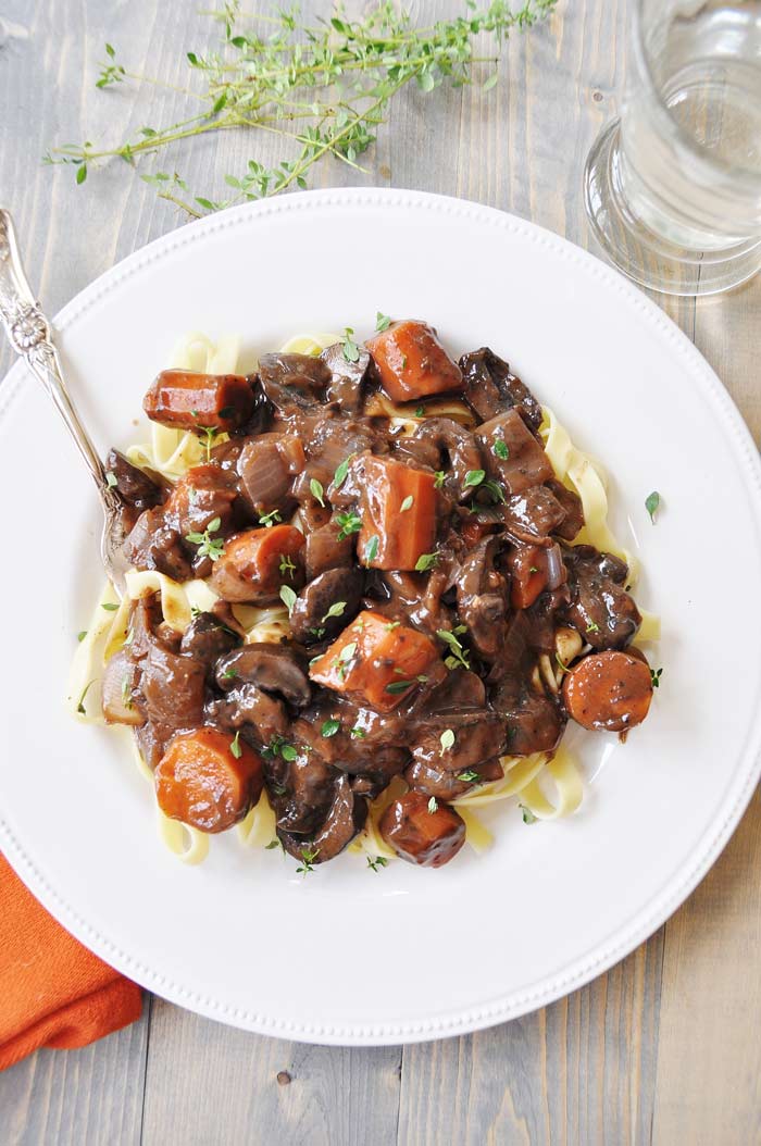 Mushroom Fourguignonne on a white plate with a silver fork and an orange napkin tucked under the bottom left corner of the plate.