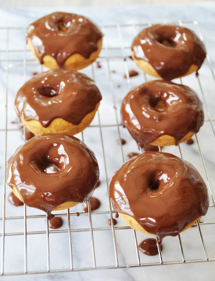 6 Baked Vegan Pumpkin Spice Doughnuts with Chocolate Cinnamon Icing on a wire rack on a marble board