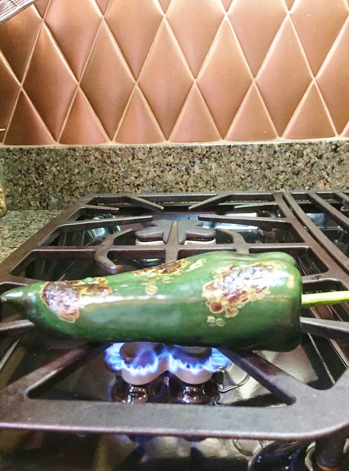 A jalapeno pepper roasting on a gas stove