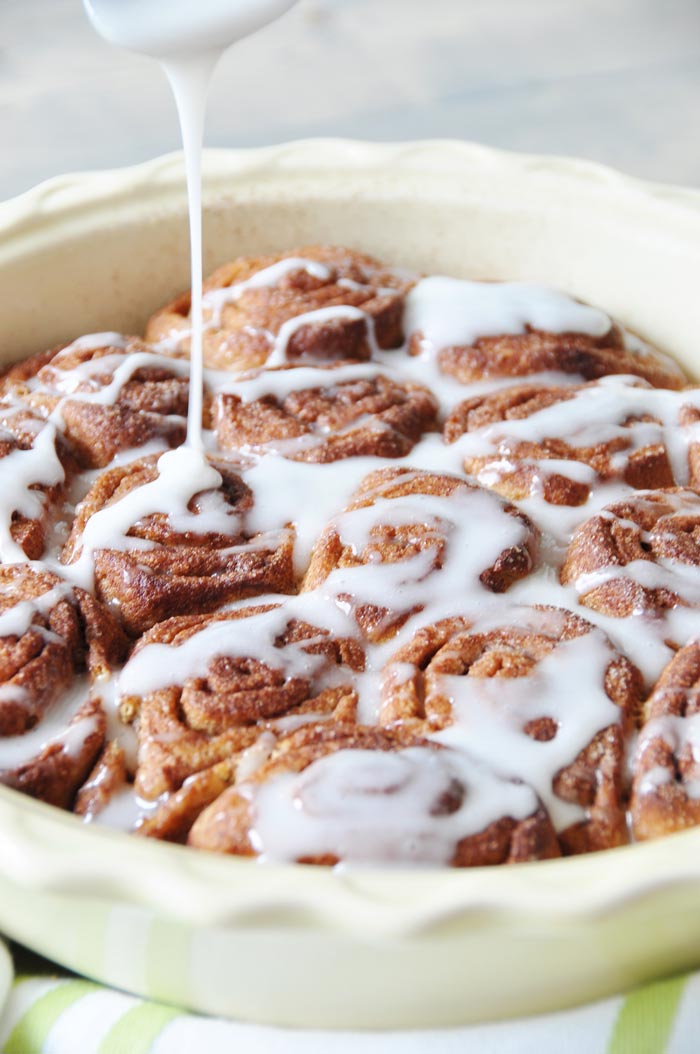 Homemade Vegan Cinnamon Rolls being drizzled with glaze in a yellow pan