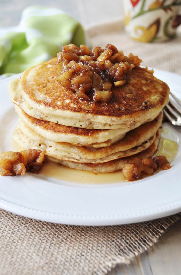 Old Fashioned Fluffy Vegan Pancakes stacked on a white plate with apple compote piled on top and on the plate