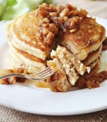 A stack of pancakes topped with syrup and chunky apples and a fork with the pancakes on it.