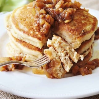 A stack of pancakes topped with syrup and chunky apples and a fork with the pancakes on it.