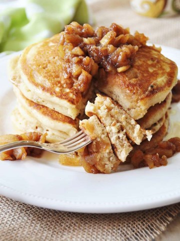 A stack of pancakes topped with syrup and chunky apples and a fork with the pancakes on it.
