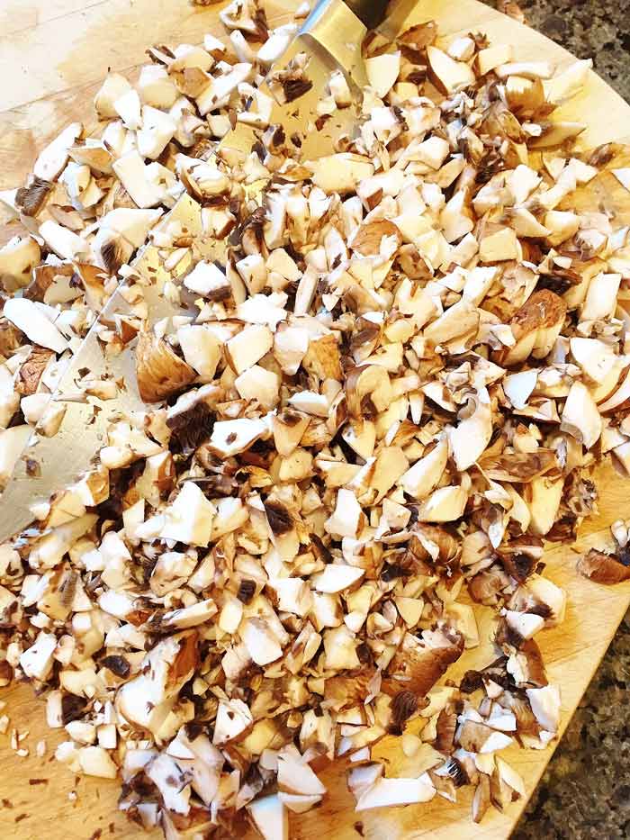 Finely-Chopped-Mushrooms on a wood cutting board with a chef's knife