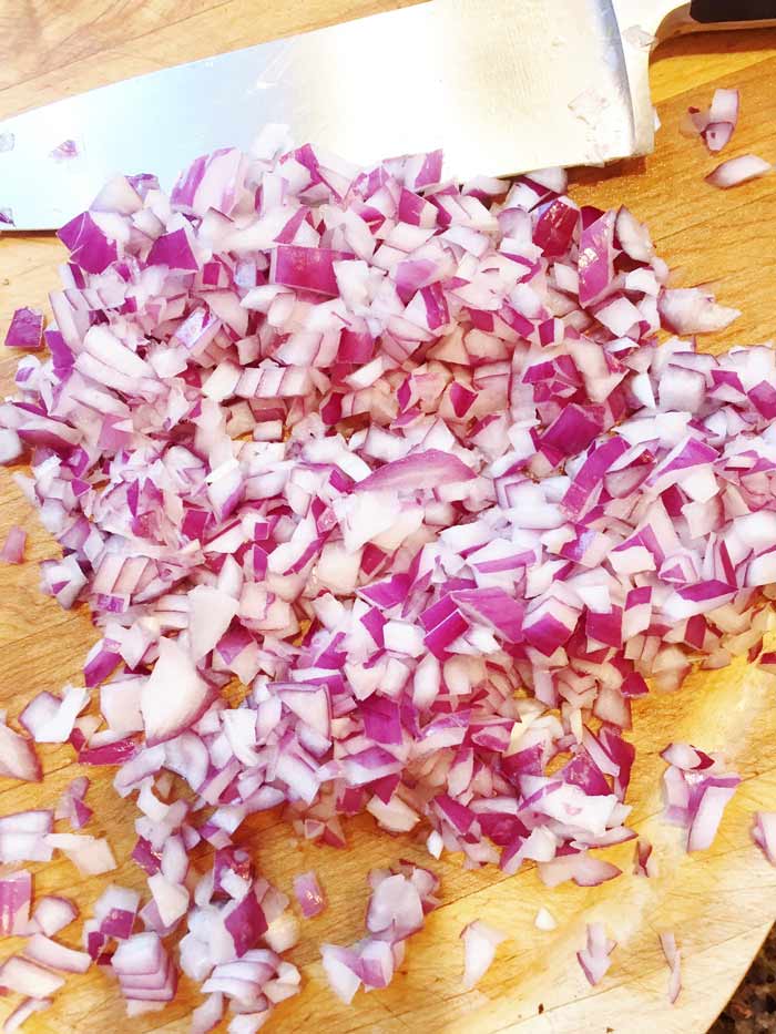 Finely-Chopped-red onions on a wooden cutting board with a chef's knife