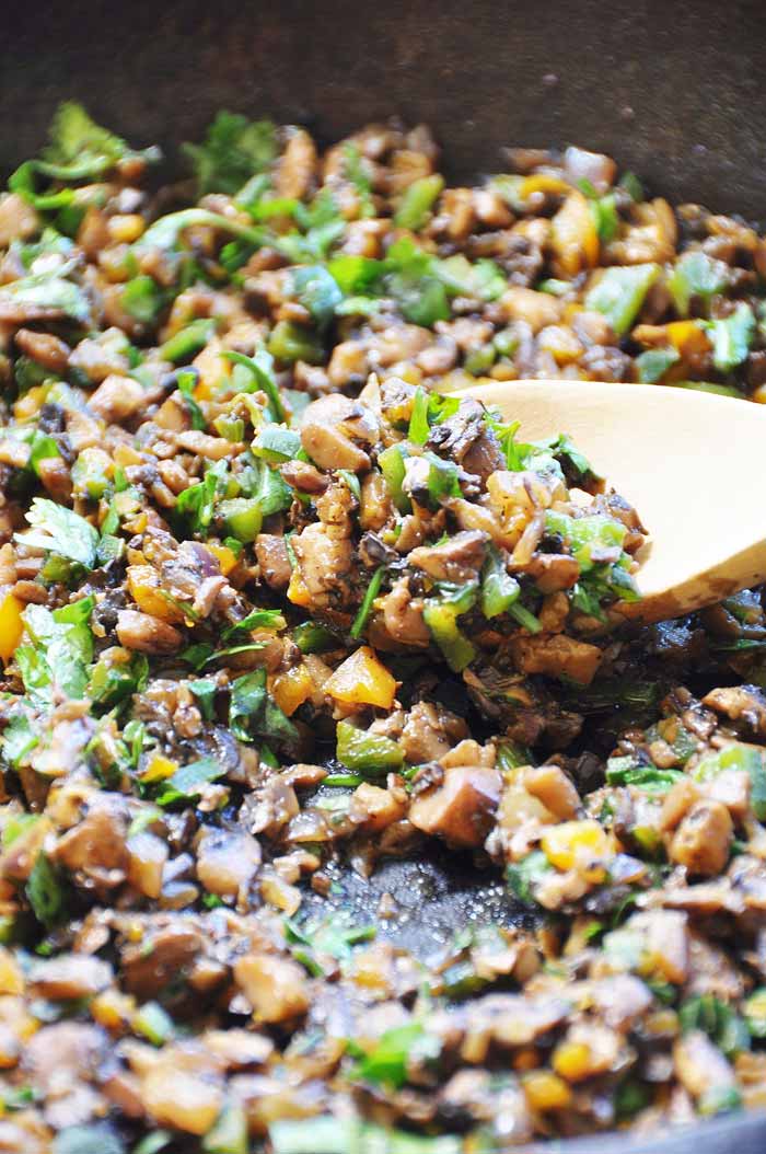 Mushroom tinga in a cast-iron skillet being scooped up with a wood spoon