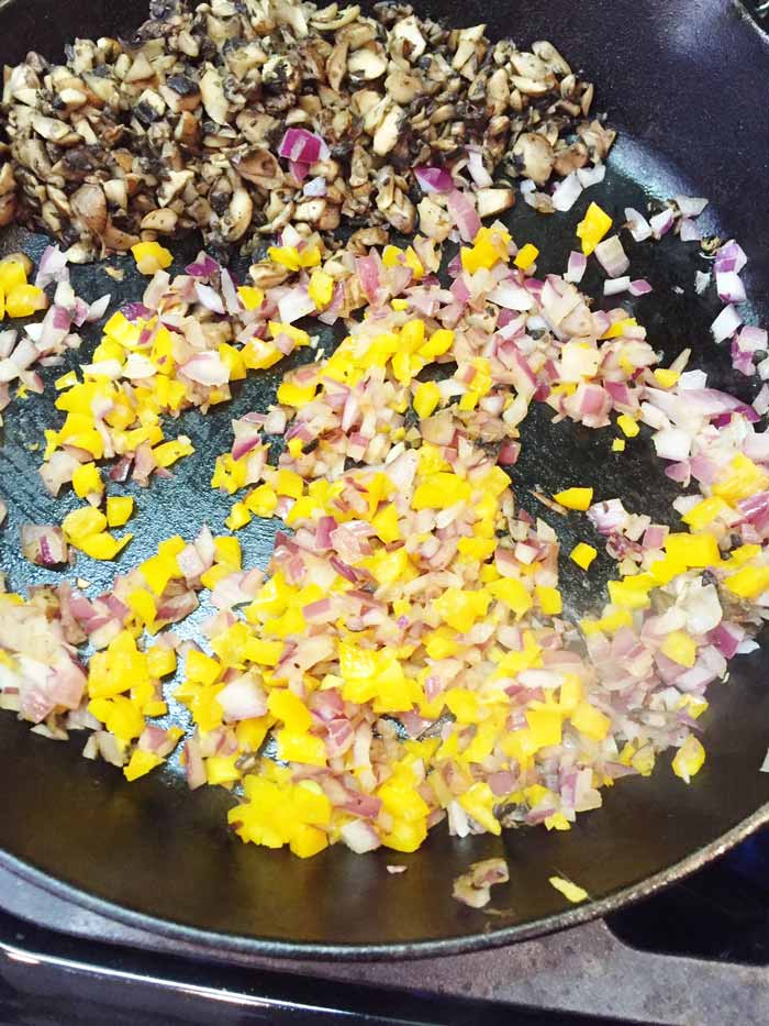 Chopped mushrooms, red onion, and yellow bell pepper cooking in a cast-iron skillet