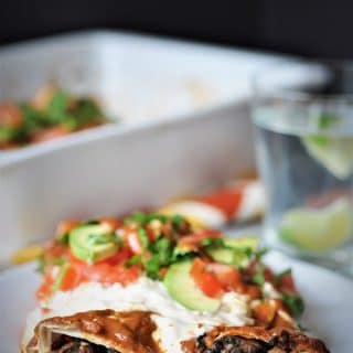 vegan black bean & mushroom enchiladas on a white plate with cashew cream sauce and sliced avocados and chopped cilantro.