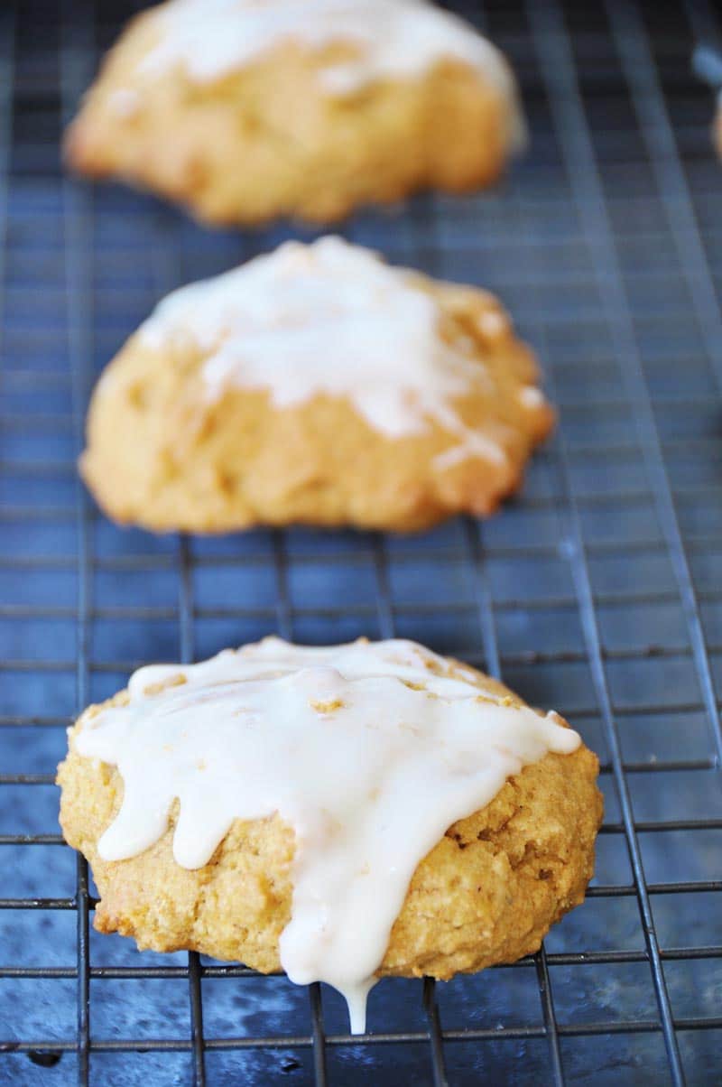 Three pumpkin cookies with glaze on a wire cooling rack.