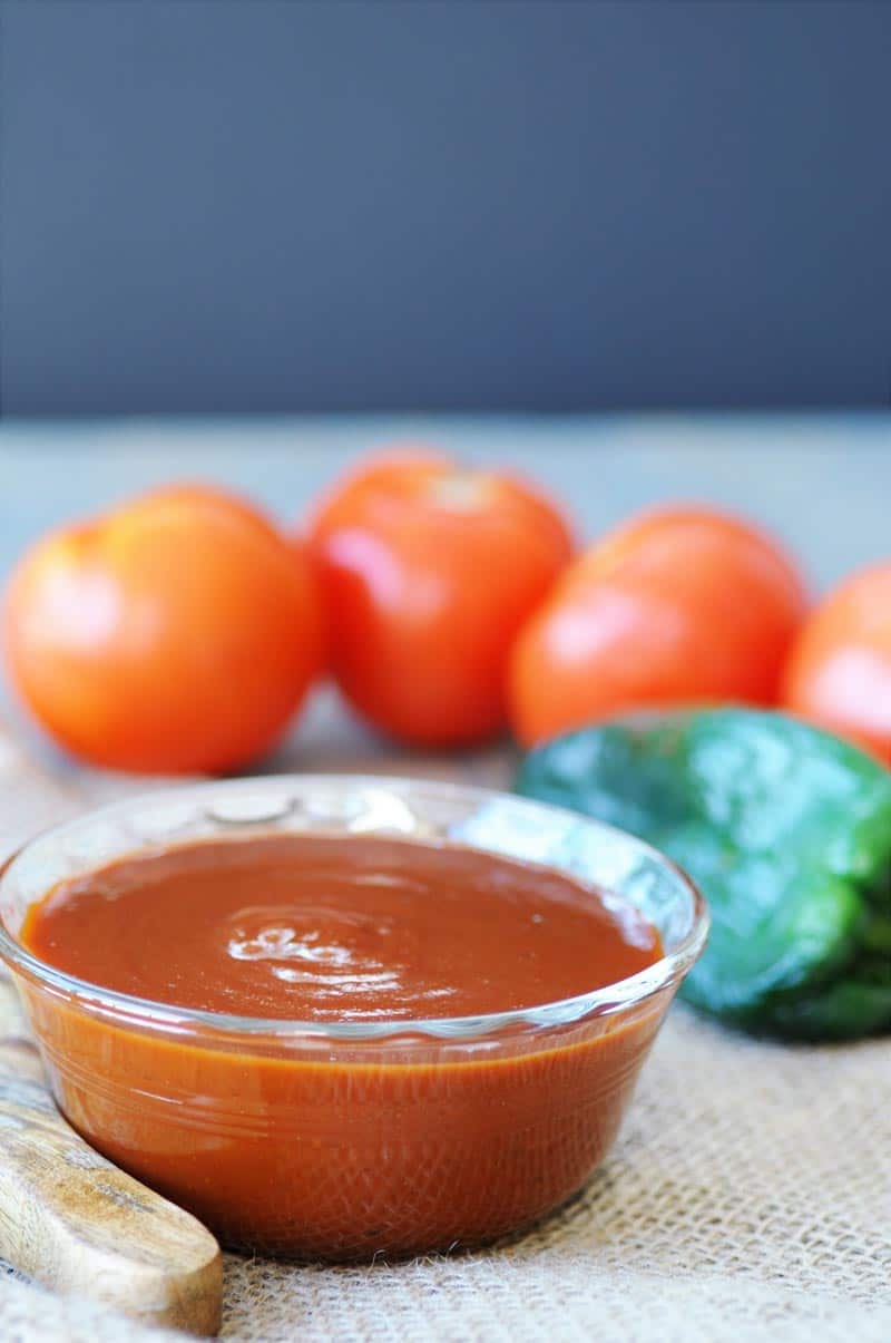 A glass bowl with BBQ sauce and tomatoes and garlic next to the bowl