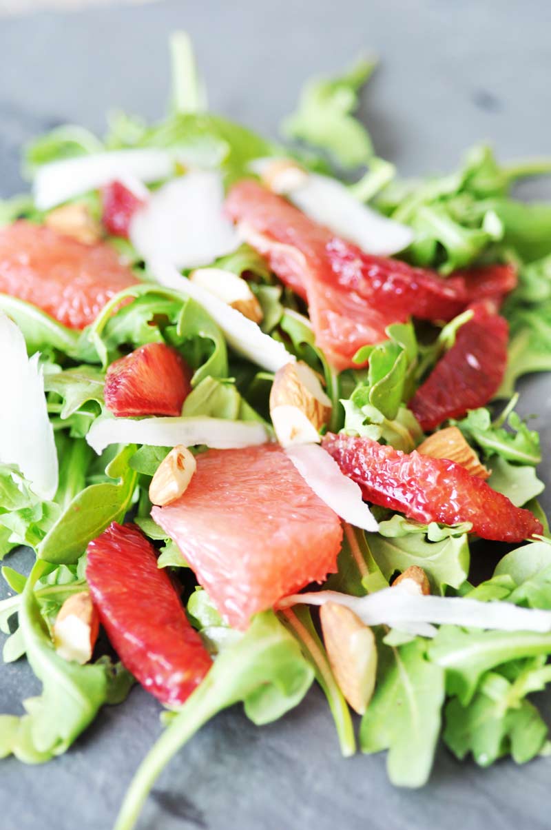 A close up shot of an arugula,, sliced citrus, and chopped almond salad. 