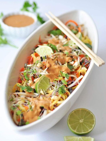 Super--Sprouts Pad-Thai-with-Spicy-Peanut-Sauce in a long white bowl with a pair of chopsticks on top and a lime and a the peanut sauce in a small white bowl in the background.