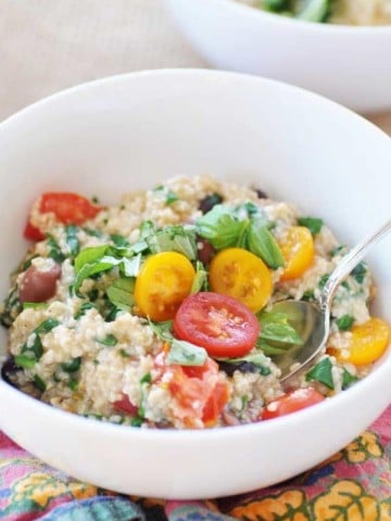 A white bowl with oats, tomatoes, and spinach with a spoon sticking out of the bowl.