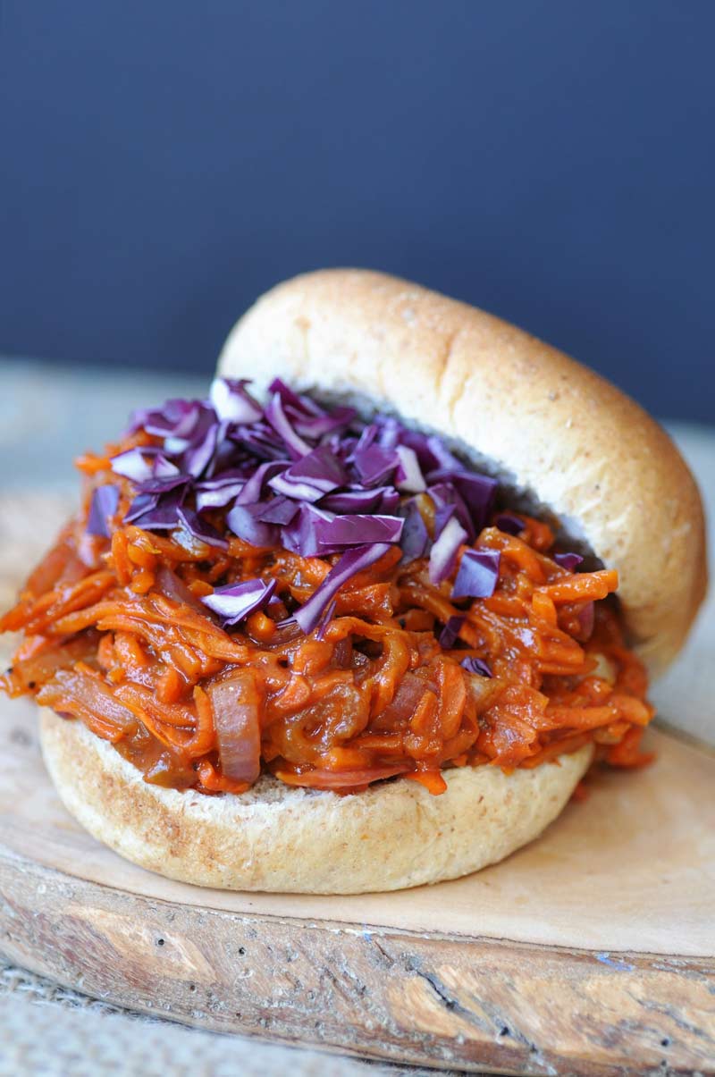 A pulled BBQ carrot sandwich with purple slaw on a bun on a wood board.