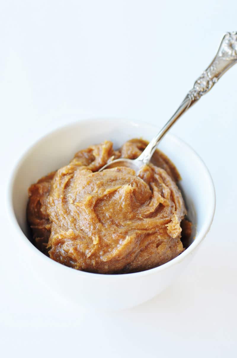 3 Ingredient Date Caramel in a white bowl with a silver spoon in the bowl on a white board