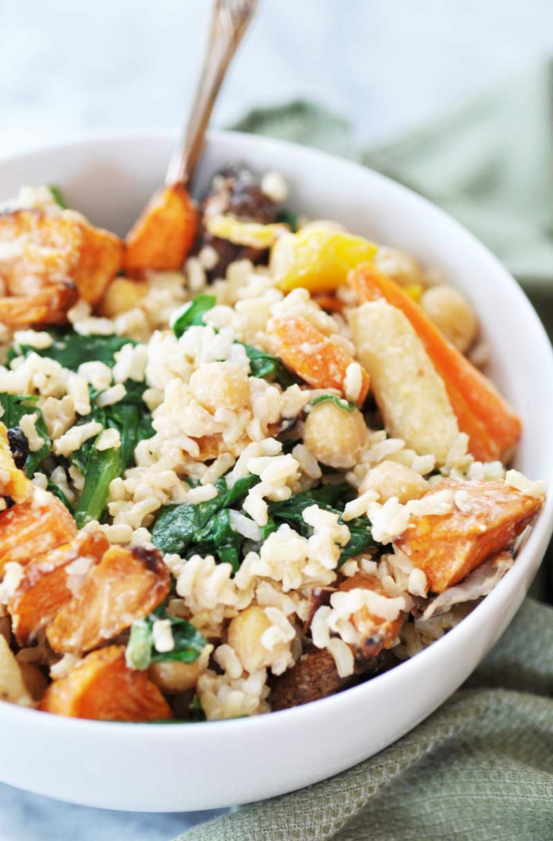 roasted vegetables with rice and tahini dressing in a white bowl with a silver fork stuck in the bowl