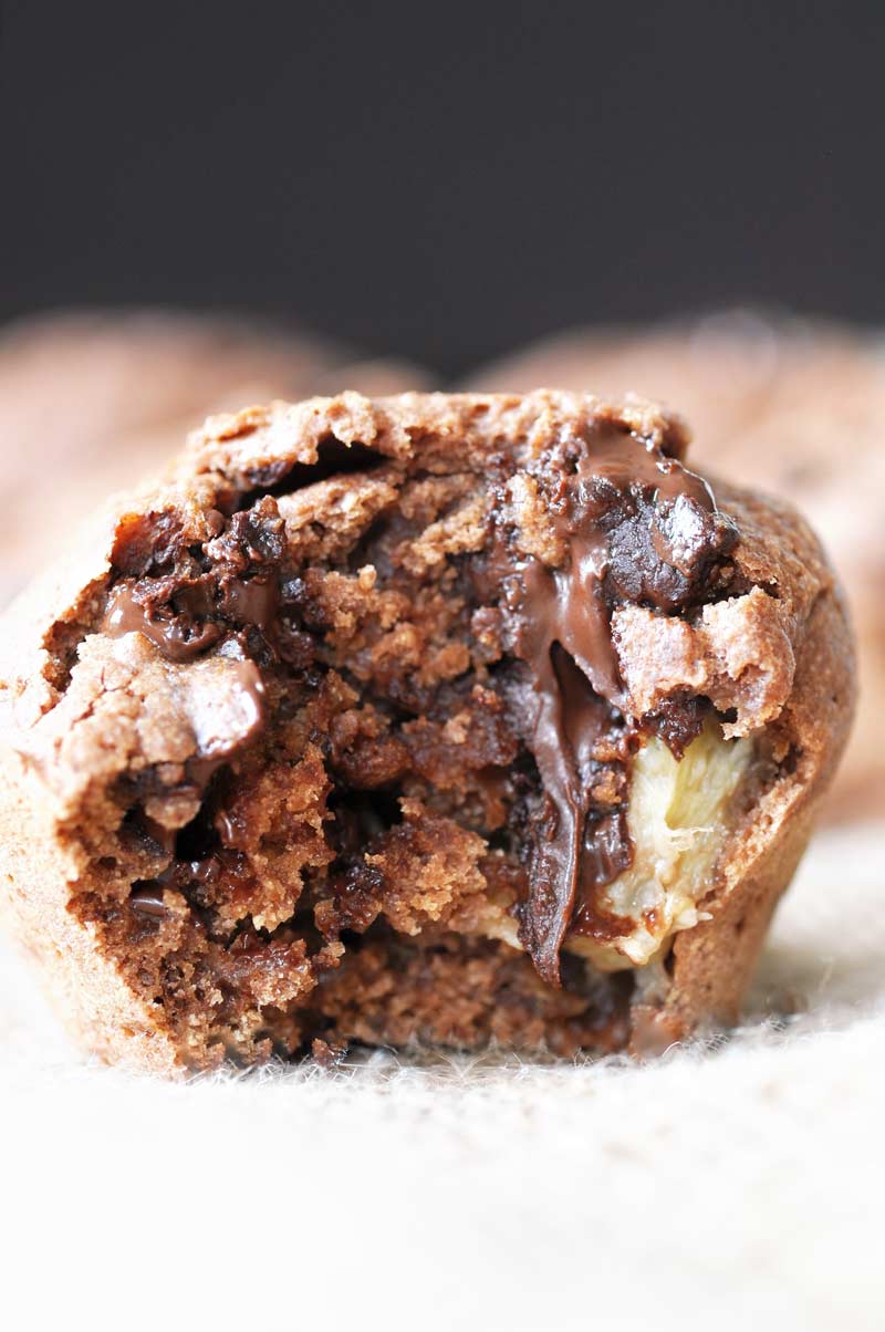 A chocolate banana muffin with a bite taken out of it and chocolate dripping down the muffin. 