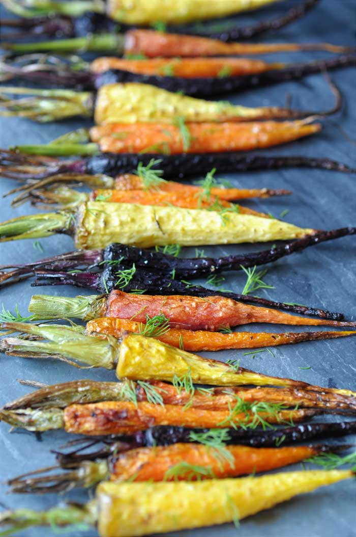 Roasted tri-color carrots on a gray slate board.