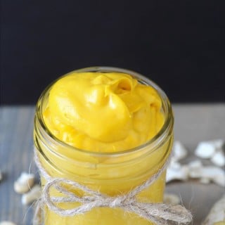 A mason jar with a string tied around it filled with cheddar cheese, and pieces of cashews sprinkled around the jar. sauce,