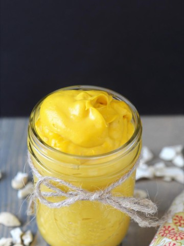 A mason jar with a string tied around it filled with cheddar cheese, and pieces of cashews sprinkled around the jar. sauce,