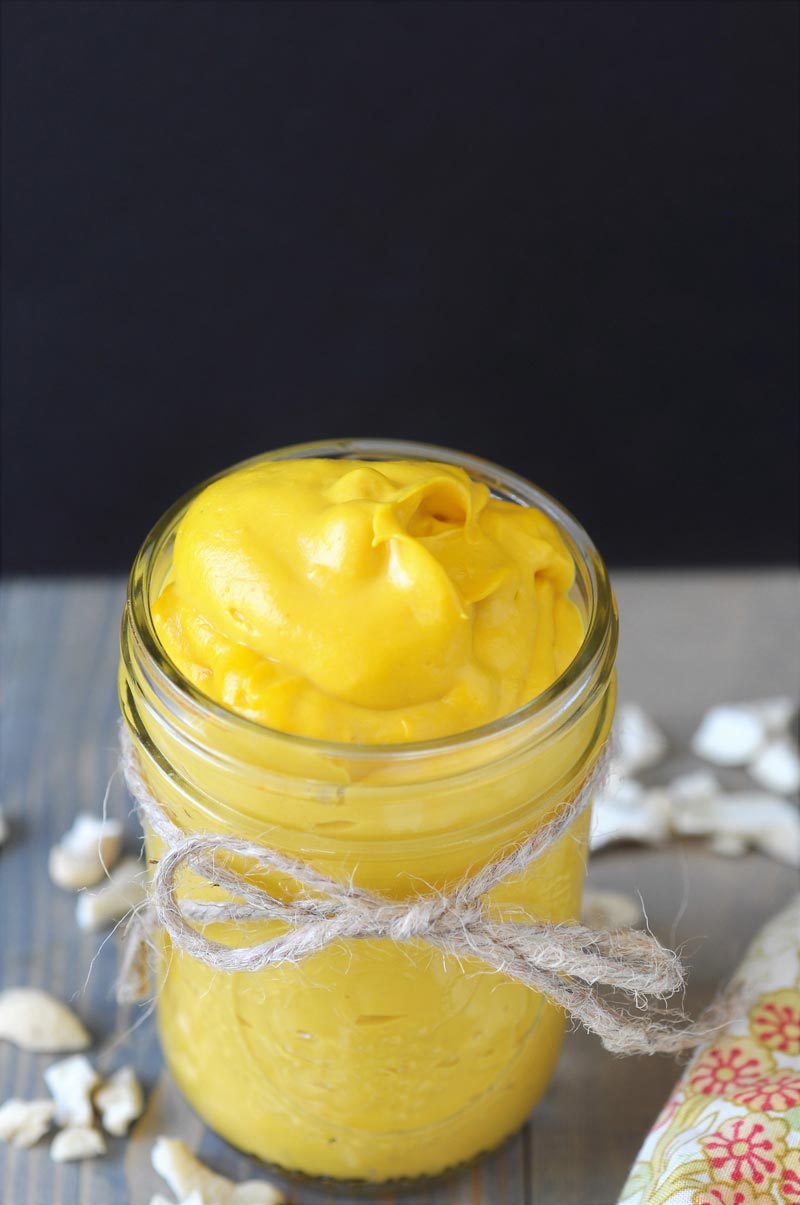 A mason jar with a string tied around it filled with cheddar cheese, and pieces of cashews sprinkled around the jar.  sauce,