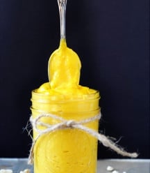 A mason jar with a string tied around it, filled with cheddar cheese sauce and a silver spoon above it with the sauce clinging to it.