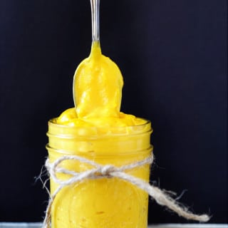 A mason jar with a string tied around it, filled with cheddar cheese sauce and a silver spoon above it with the sauce clinging to it.