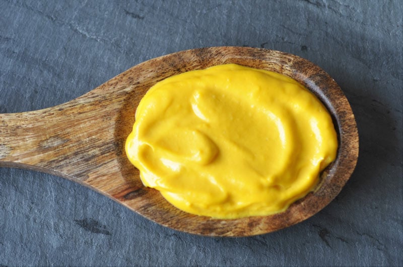 A wooden spoon with cheddar cheese sauce, laying on a piece of gray slate.