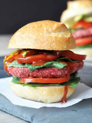 A veggie beet burger with lettuce and tomato and ketchup dripping down the side.