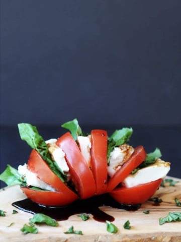 Single Serving Vegan Caprese Salad on a wood board with chopped basil sprinkled around on it and a black background