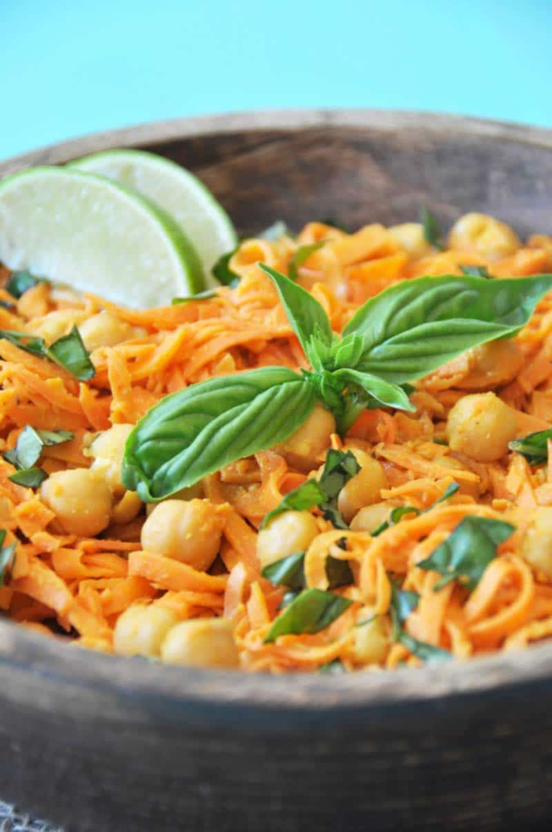 Sweet potato noodles and chickpeas with basil in a wooden bowl with 2 lime wedges garnishing the side of the bowl. 