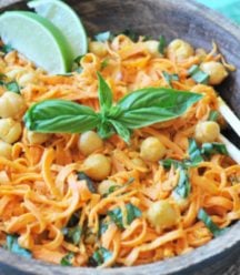 A wooden bowl with spiralized sweet potatoes, chickpeas, and basil with a pair of chopsticks in the bowl.
