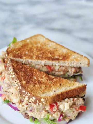A tuna salad sandwich on toast, cut in half on a white plate.